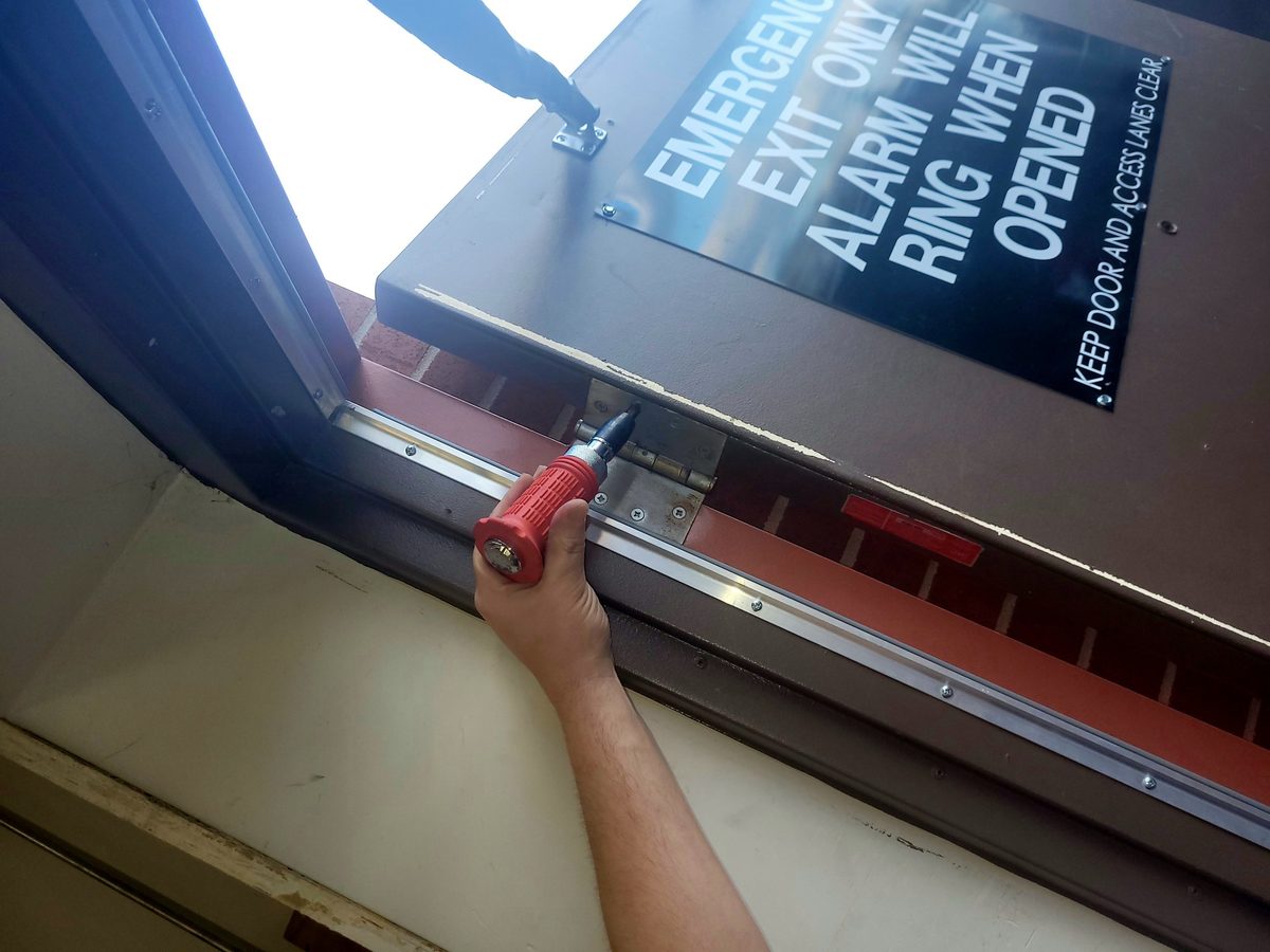 Drill fastening a new sweep and weatherstrip to the bottom of a commercial exit door in Greenwood