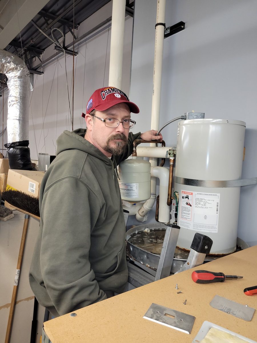 Nicholas Studebaker working on a plumbing repair at a utility sink in Greenwood